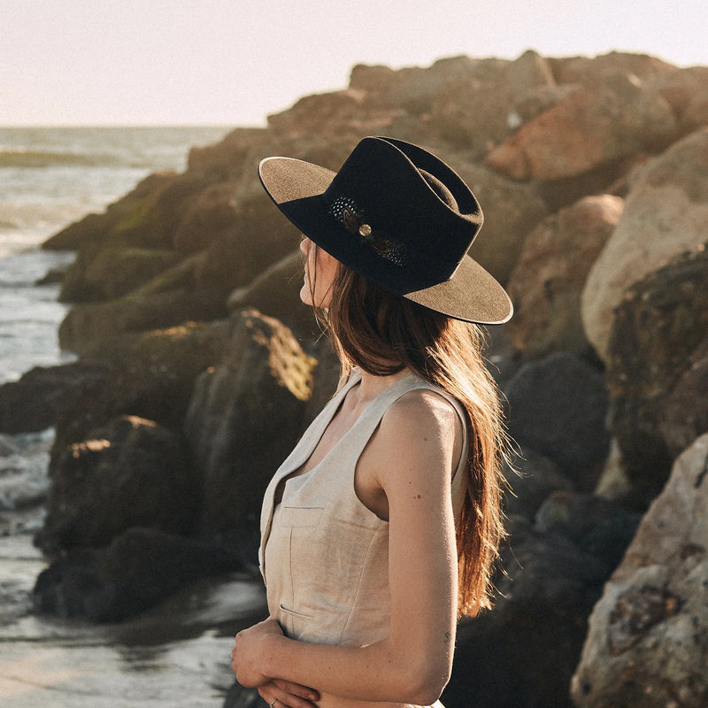 Woman wearing a black cowboy hat by the ocean with rocks in the background