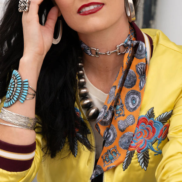 Woman wearing a yellow jacket with floral embroidery, an orange scarf, and silver jewelry.