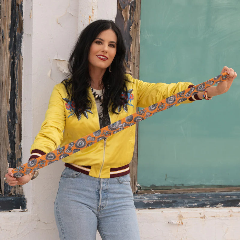 Woman wearing a yellow jacket with floral patterns, standing against a textured wall.