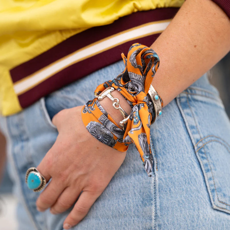 Person wearing a colorful scarf as a bracelet with denim jeans and a yellow jacket.