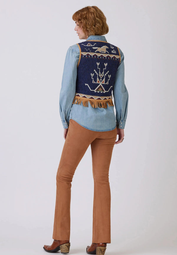Woman wearing goat suede vest, completely covered in intricate hand-beading depicting classic pictorials of the Plains and Southwestern shapes and symbols, complemented by cowrie shells and finished with fringe and a 3-tie tassel closure..