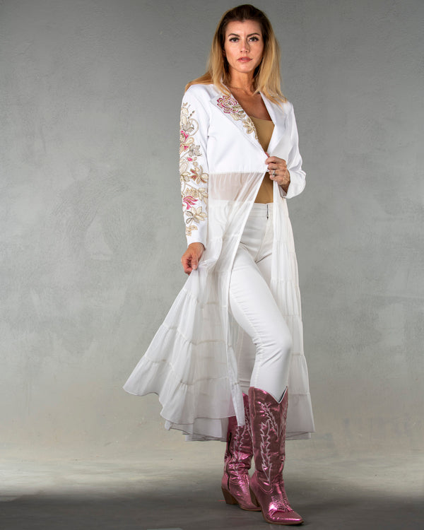 Woman wearing long white duster with long sleeves and multicolor floral embroidery 