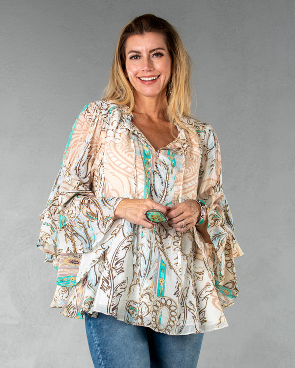 Woman wearing flowy long sleeve top in a cream, white, brown, and turquoise colorway representing an ornate pattern 