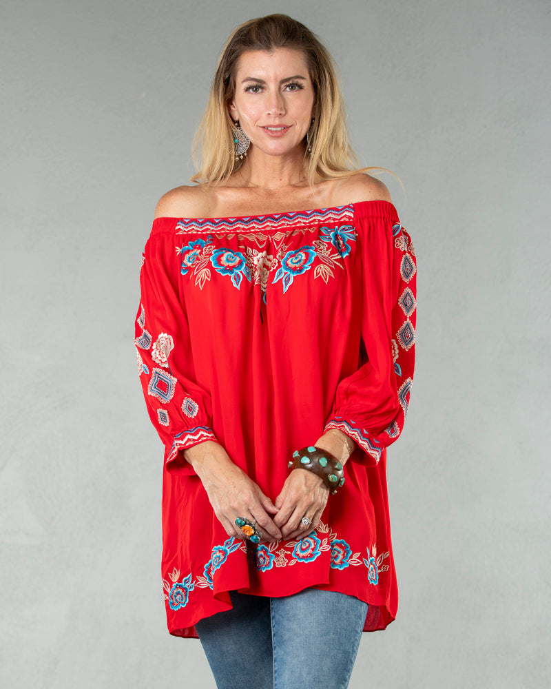 Woman wearing vibrant red long sleeve, off the shoulder tunic with multicolor floral and tribal embroidery detail on chest, sleeves and hemline
