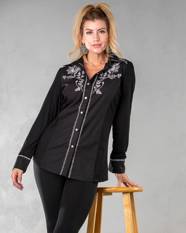 Woman wearing black long sleeve button front top with white embroidery floral and roping detail