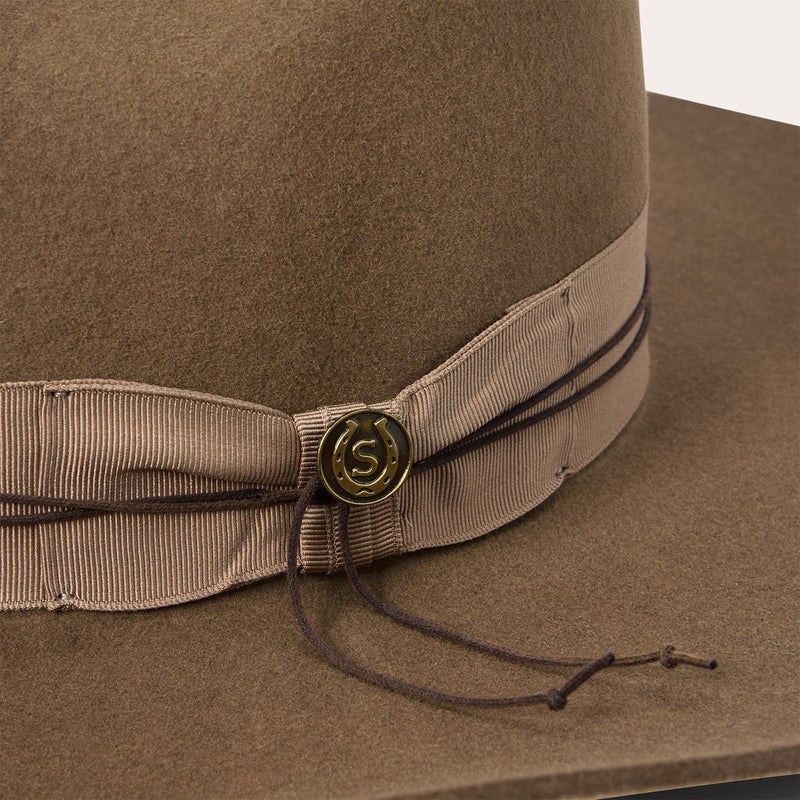 Brown hat with a ribbon and button detail on a white background