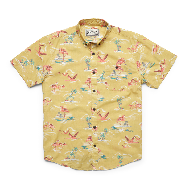 Yellow short sleeve button down shirt with pink flying flamingos and stationary flamingos standing in water near palm trees throughout
