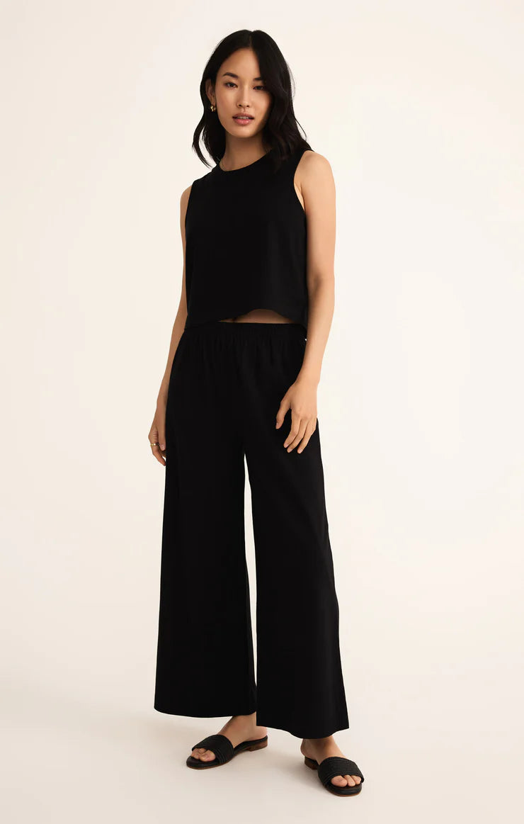 Woman wearing a black sleeveless top and wide-leg pants on a beige background