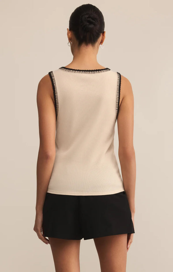 Woman wearing a beige sleeveless top with black trim and black shorts on a beige background