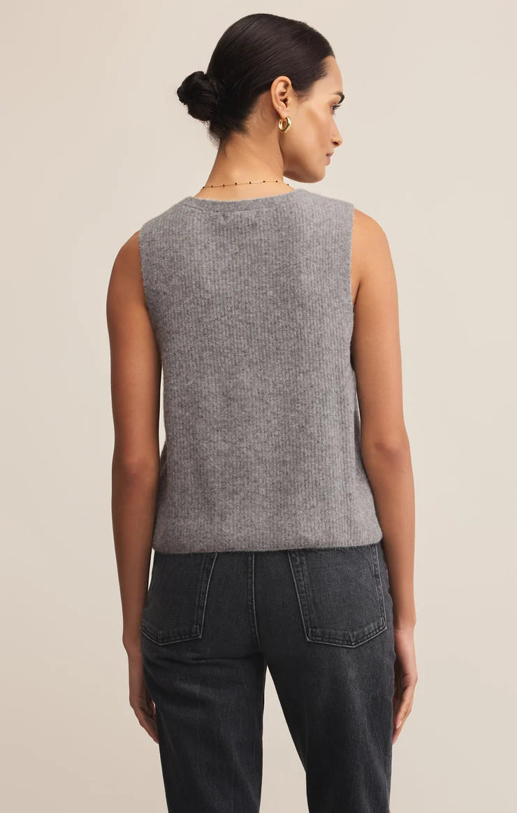 Woman wearing a gray sleeveless top and dark jeans on a beige background