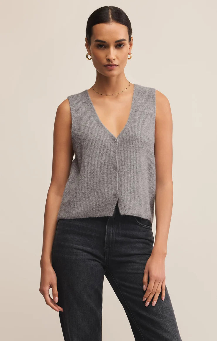 Woman wearing a gray sleeveless sweater vest and black pants on a beige background
