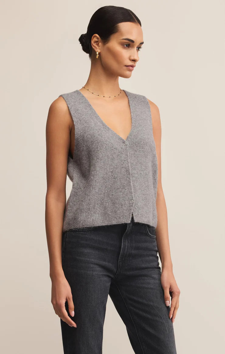 Woman wearing a gray sleeveless top and dark jeans against a beige background