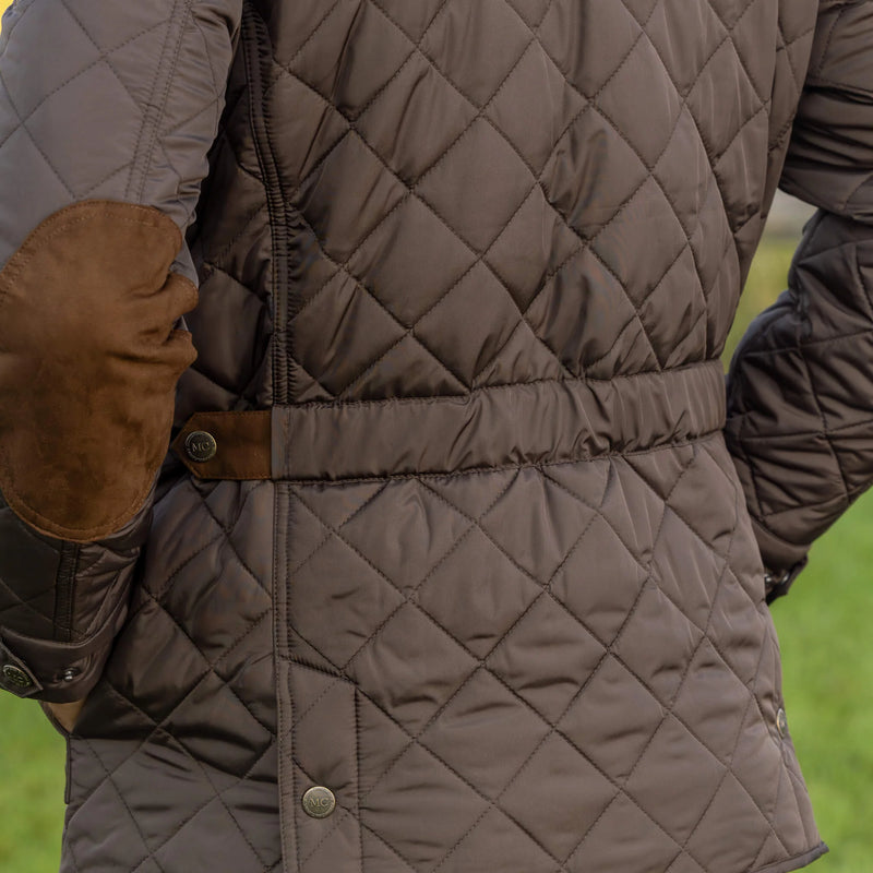 Quilted brown jacket with leather gloves on a blurred green background
