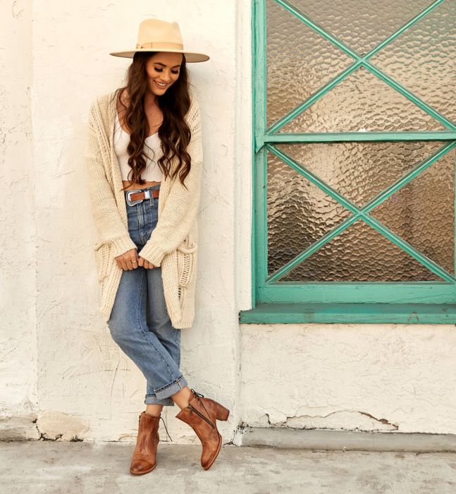 smiling lady with cowboy hat in jeans and long cardigan wearing a tan leather bootie with 2.5 inch heels
