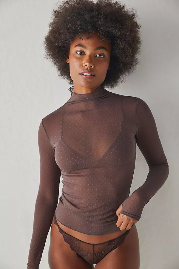 Woman wearing sheer long sleeve top that features dotted details and a high neckline.