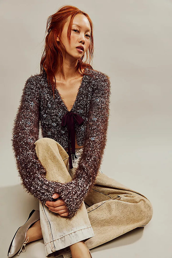 Woman wearing fuzzy fabrication, cropped fit sweater with bow-tie detailing at the front and embellished detail throughout.