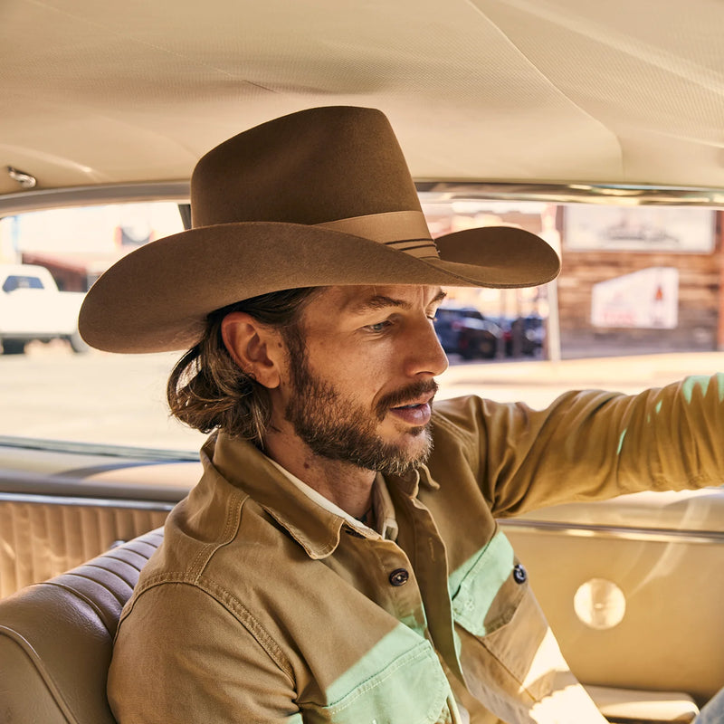Man wearing a cowboy hat and beige jacket sitting inside a vehicle.