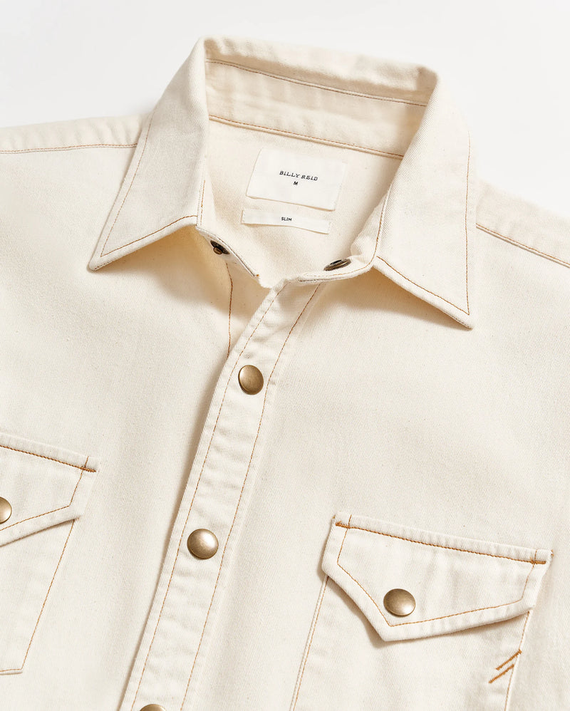MAN WEARING CREAM BUTTON UP SHIRT WITH BRASS BUTTON SNAPS AND DOUBLE BREAST POCKETS