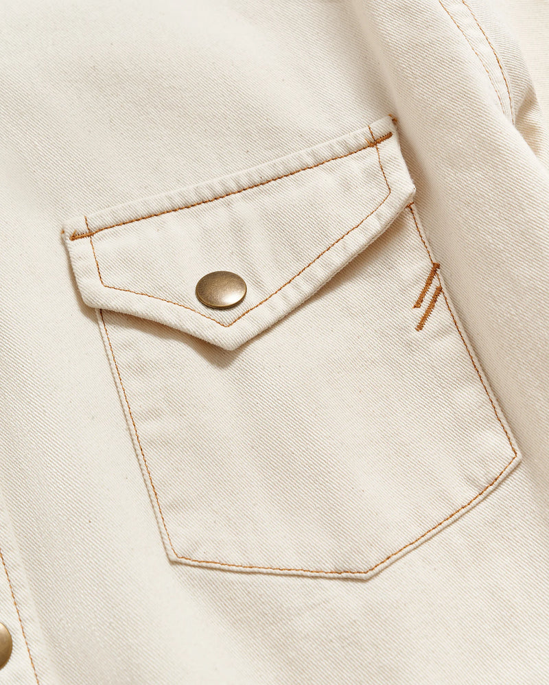 MAN WEARING CREAM BUTTON UP SHIRT WITH BRASS BUTTON SNAPS AND DOUBLE BREAST POCKETS