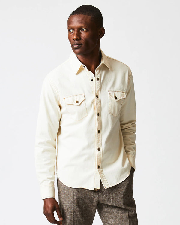 MAN WEARING CREAM BUTTON UP SHIRT WITH BRASS BUTTON SNAPS AND DOUBLE BREAST POCKETS