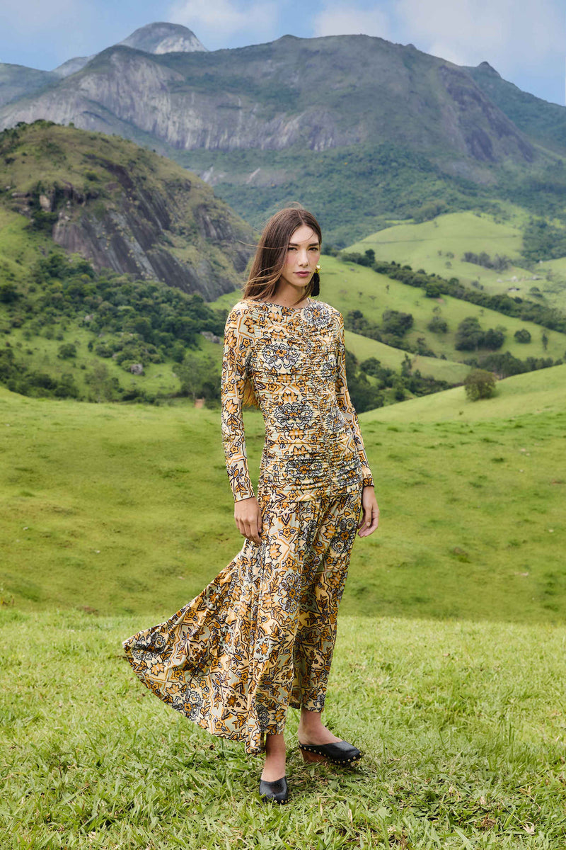 Woman in a floral dress standing in a grassy field with mountains in the background