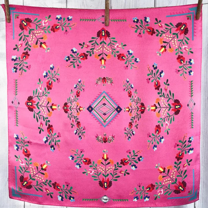 Pink fabric with colorful floral and geometric patterns hanging on a wooden surface.