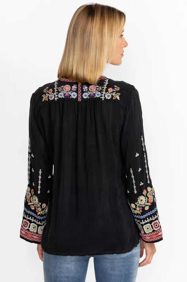 Woman wearing blouse that boasts a tie at the neckline with tassels, long sleeves, and a detailed placement embroidery in rich shades