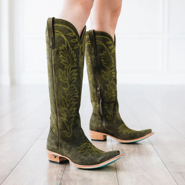 Green cowboy boots with detailed patterns worn by a person on a light wooden floor.