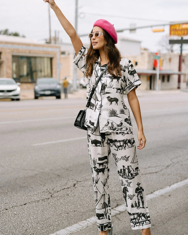 Woman wearing white pj with black images of teepees, the Prada store in Marfa, snakes, horses, cacti, cattle and a cowboy