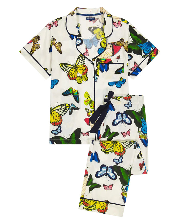 Woman wearing white background pajamas with vibrant, multicolor butterflies all over. The top is a short sleeve and the bottoms are long pants
