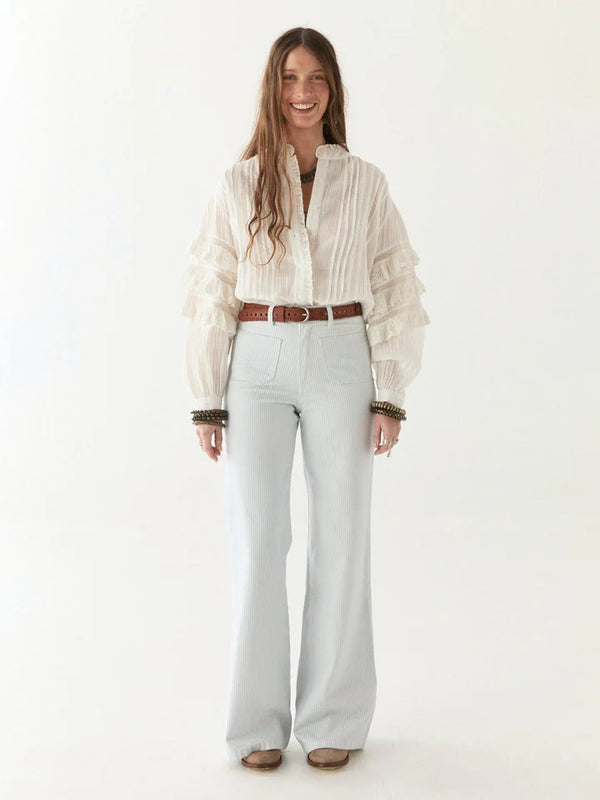 Woman wearing a light-colored blouse and light blue jeans on a white background