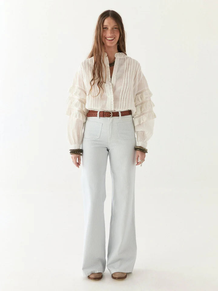 Woman wearing a light-colored blouse and light blue jeans on a white background