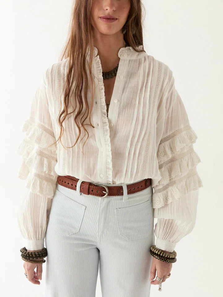 Woman wearing a white blouse with ruffled sleeves and a belt, standing against a white background