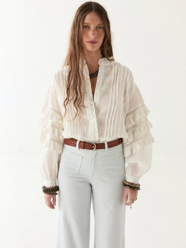 Woman wearing a white blouse with ruffled sleeves and light blue jeans on a white background