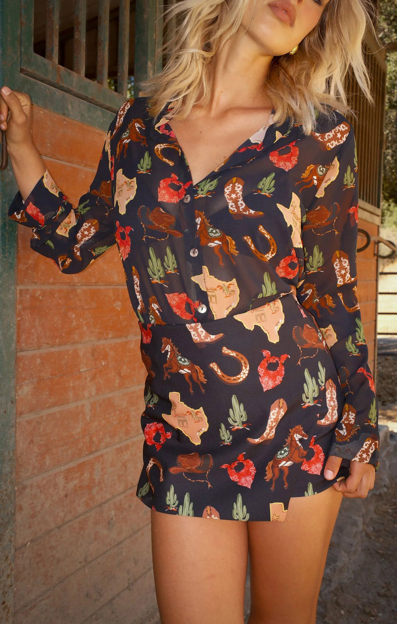 Woman wearing a patterned dress with long sleeves in front of a brick wall.