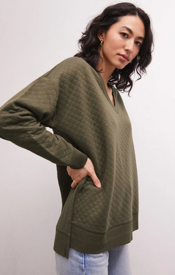 Woman wearing quilted army green v neck top with side slits on the bottom hem.