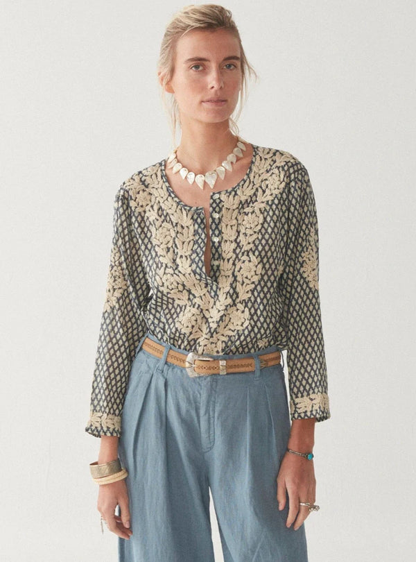 Woman wearing long sleeve blouse with blue and cream pattern with cream embroidery leaves all over