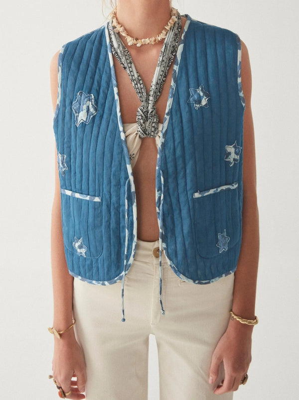 Woman wearing quilted blue vest with stars on one side and floral pattern on the other. This item is reversible 