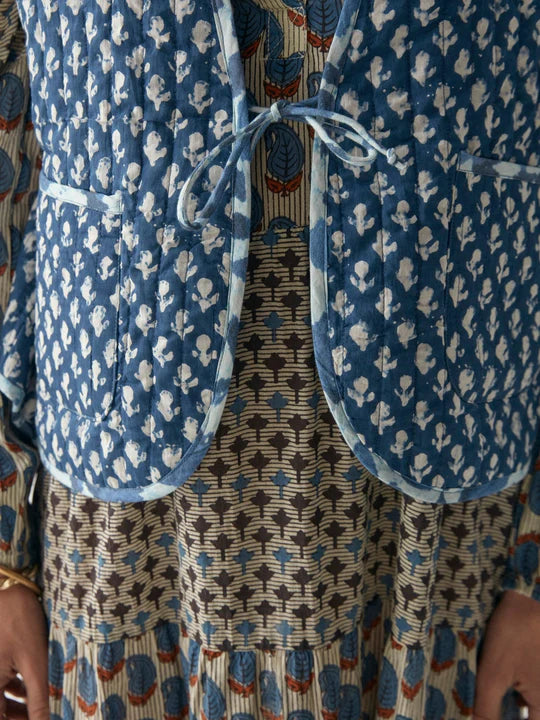 Woman wearing quilted blue vest with stars on one side and floral pattern on the other. This item is reversible
