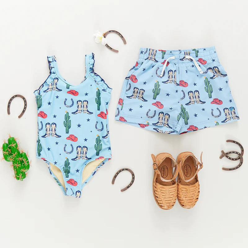 Little girls swimsuit with blue background, images of boots, cacti, stars and hats all over with ruffle straps