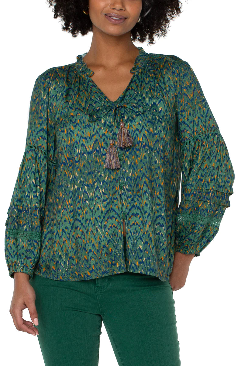 Woman wearing emerald green blouse with deep blue, orange and gold pattern throughout 