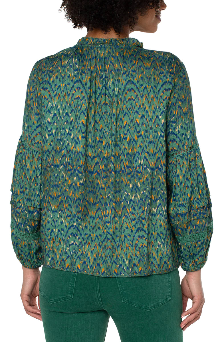 Woman wearing emerald green blouse with deep blue, orange and gold pattern throughout