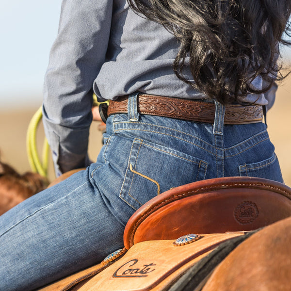 Person wearing a brown leather belt with intricate designs, sitting on a horse with a Conti saddle.