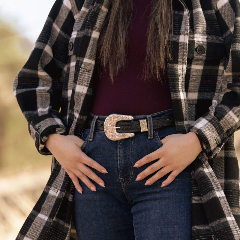 Person wearing a black and white plaid shirt over a purple top, with blue jeans and a decorative belt.