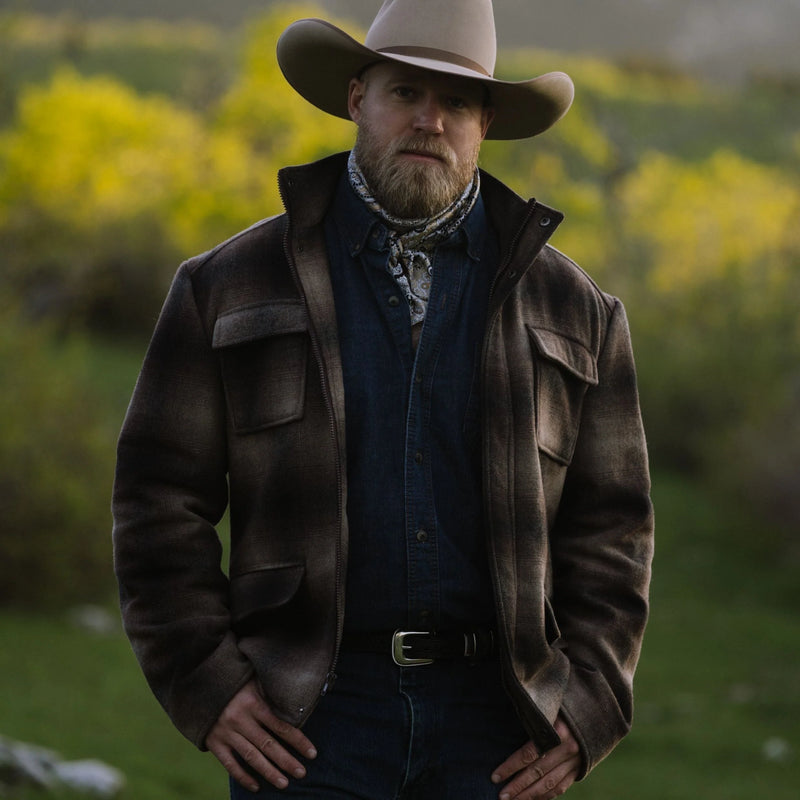 Man wearing a cowboy hat and leather jacket standing in a field
