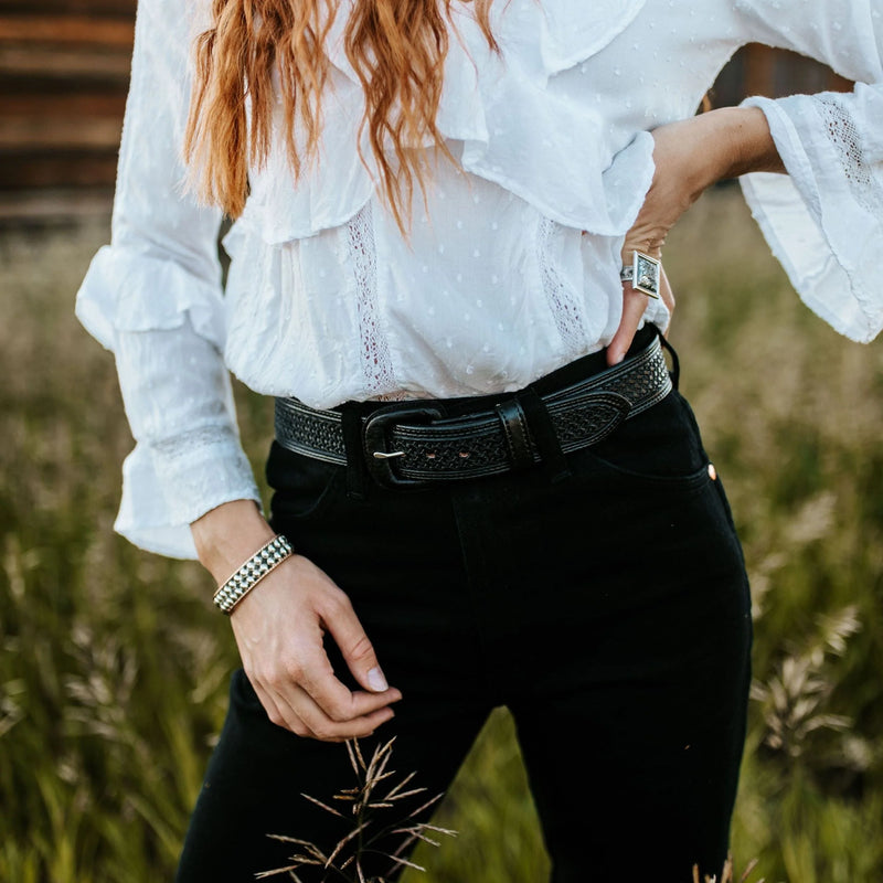Person wearing a white blouse with ruffled sleeves and black pants in a natural setting.