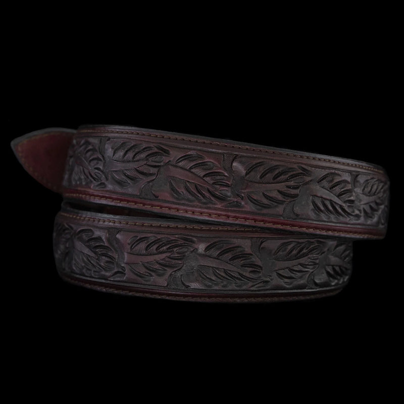 Brown leather belt with intricate leaf pattern on a black background