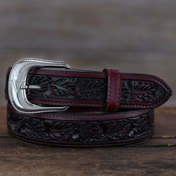 Brown leather belt with intricate designs and a silver buckle on a wooden surface.