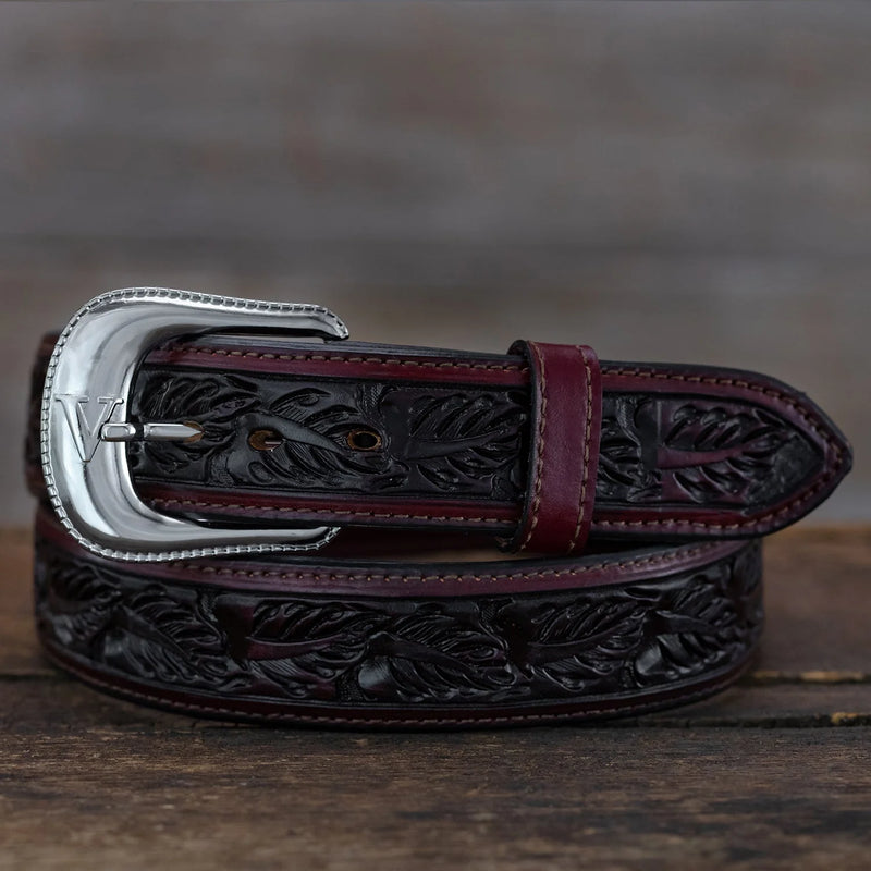 Brown leather belt with intricate designs and a silver buckle on a wooden surface.