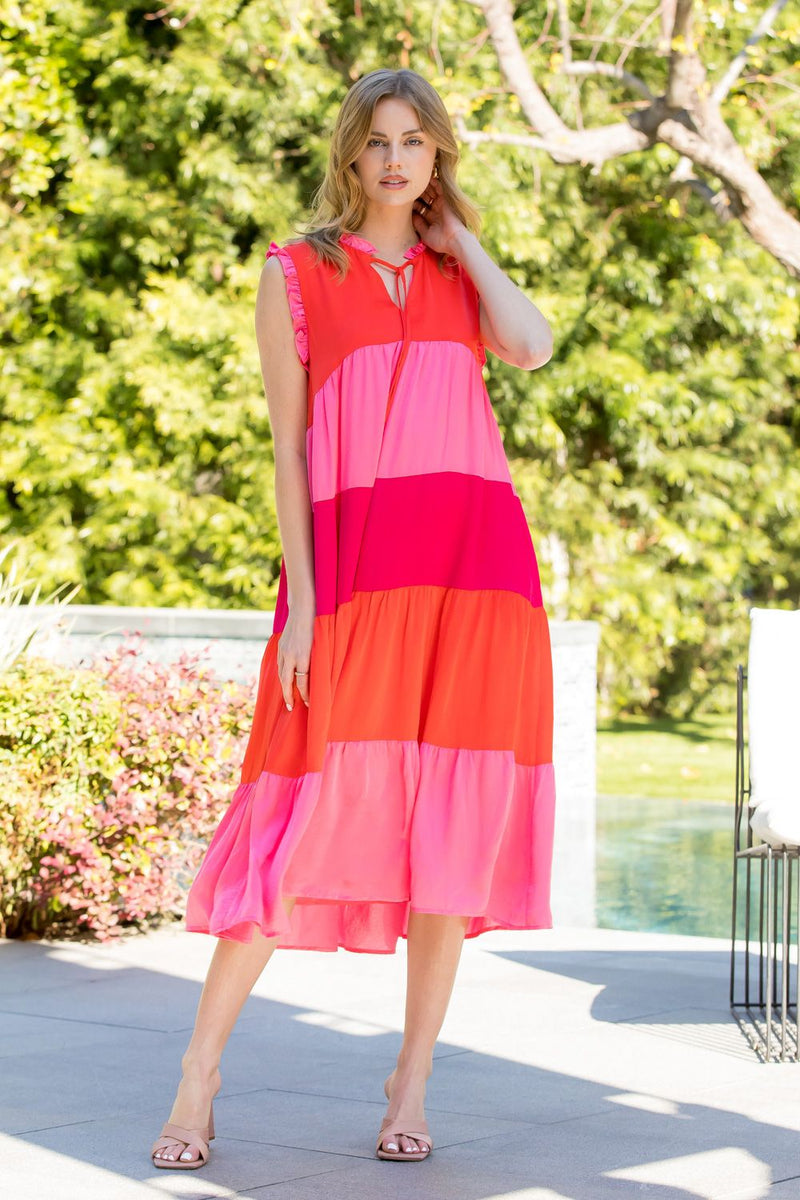 Woman wearing pink and red midi length tiered dress with v-neck and tie on neck
